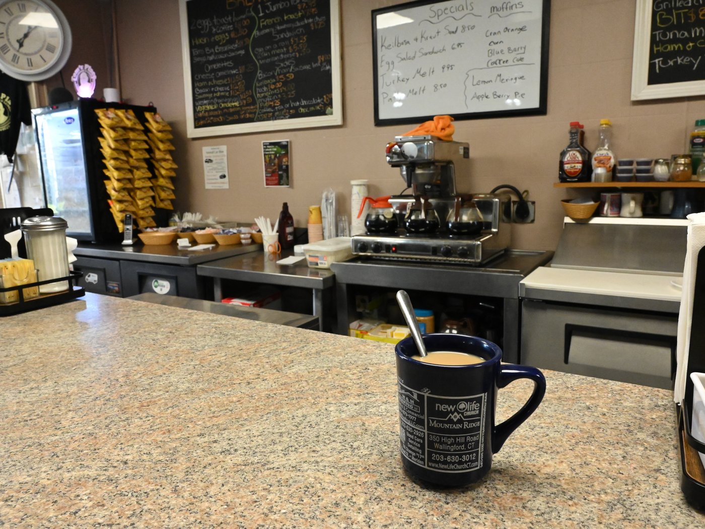 A mug of coffee on the counter, chalkboard menus behind
